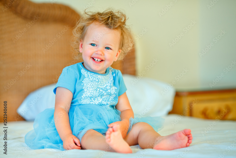 Fototapeta premium Lovely happy blonde toddler girl sitting on a bed