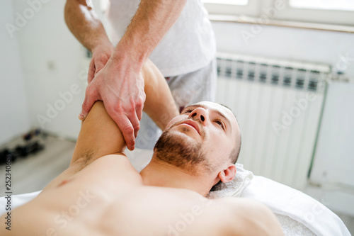 Slika na platnu Male physio therapist giving sport massage to the young Man at the salon