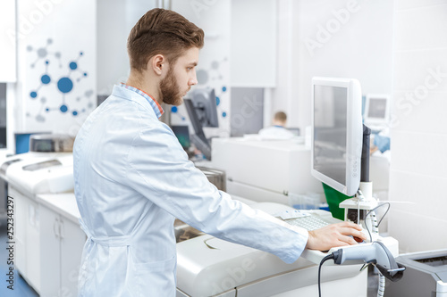 Handsome young male laboratory technician operating computerized analyzing machine