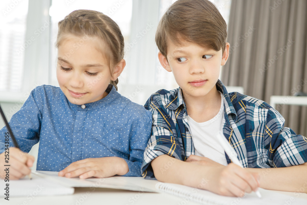 Young boy copying from his classmate during test Young boy copying from his classmate during test