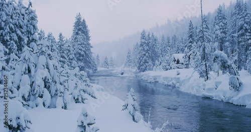 Beautiful snowy river forest scene with cabin and snowflakes falling, amazing winter nature scene