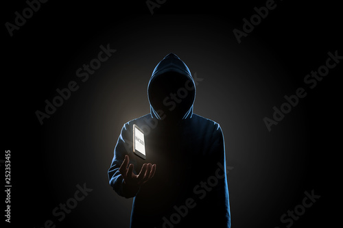 White smartphone with text "HACKER" on screen floating above of hacker's hand in dark background. Finance, business, e-commerce or cyber crime concept