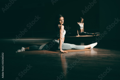 Young Caucasian flexible brunette in sportswear doing exercises on mat with spread legs. In background mirror. © dusanpetkovic1