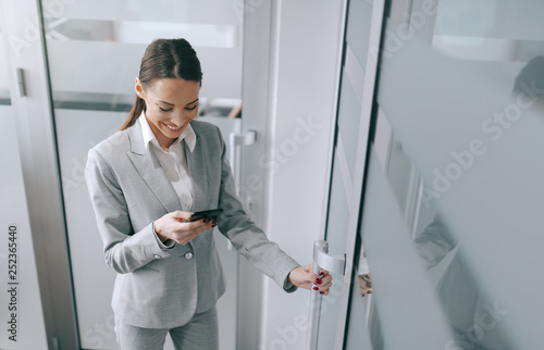Εκτύπωση καμβά Attractive Caucasian brunette in formal wear using smart phone and entering the office
