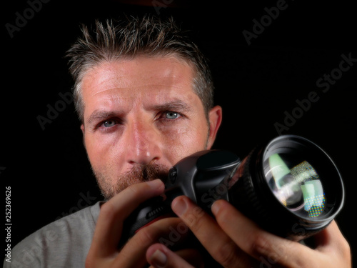 attractive and handsome man on his 30d holding professional reflex photo camera next to his face isolated on black background in photography hobby photo