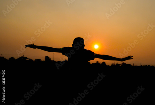 Silhouette of Asian teen boy jumping at the field with sunset background in evening.