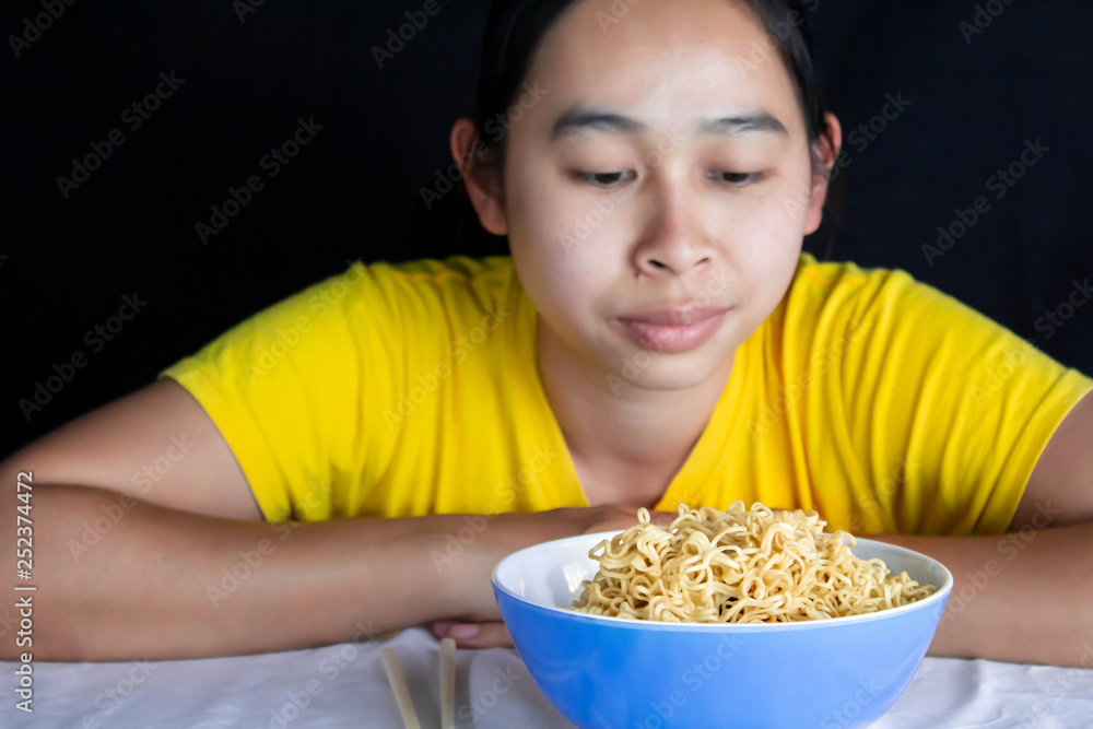 Asian woman sitting bored with instant noodles; Isolated on black background. Junk food concept. Asian woman sitting bored with instant noodles; Isolated on black background. Junk food concept.