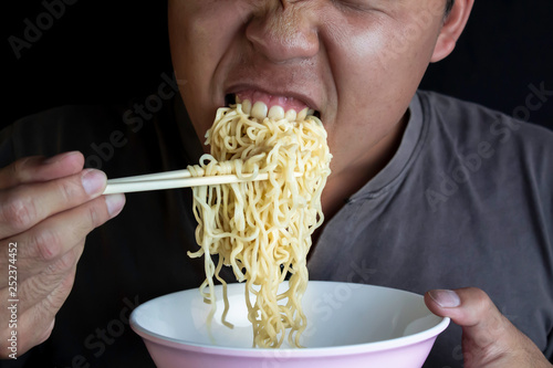 Asian Men hand uses chopsticks to pickup of instant noodles in cup and eating on dark background. Junk food concept   Sodium diet high risk kidney failure.