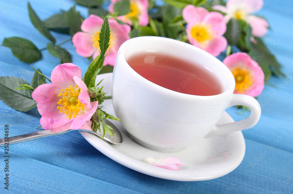 Fototapeta premium Cup of hot tea and wild rose flower on boards