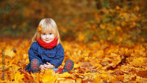 Little autumn funny girl sitting in autumn park. Selective focus  copy space.