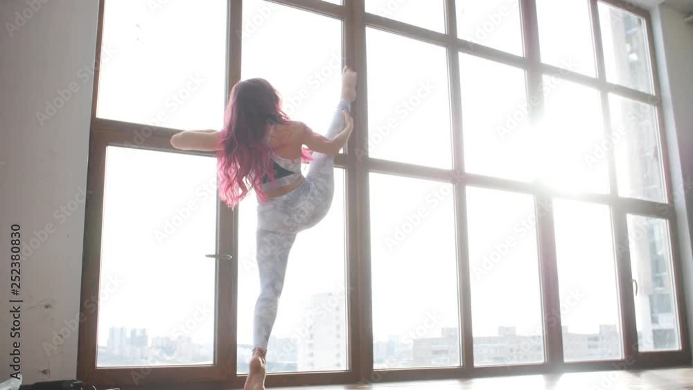 Concept of stretching and flexibility. Young woman in sportswear doing stretching near window in a white interior Concept of stretching and flexibility. Young woman in sportswear doing stretching near window in a white interior