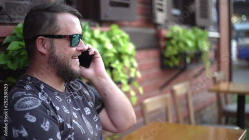 bearded man talking on the phone and chatting in a cafe on the street. 4k.