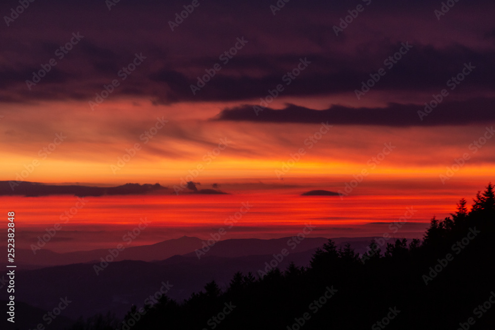 Trees silhouettes against a beautifully colored sky at dusk, with mountains layers in the background Trees silhouettes against a beautifully colored sky at dusk, with mountains layers in the background