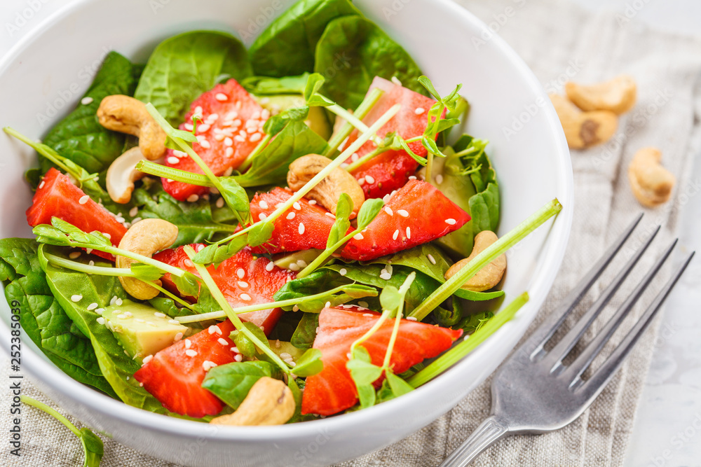 Summer strawberry avocado salad with cashews in a white bowl.