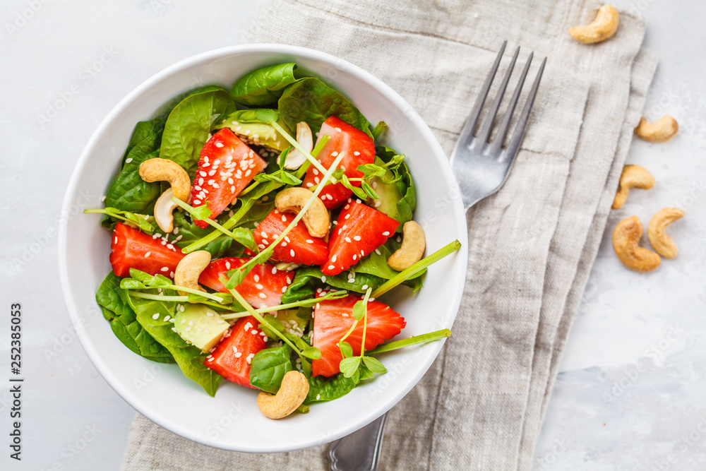 Summer strawberry avocado salad with cashews in a white bowl, top view.