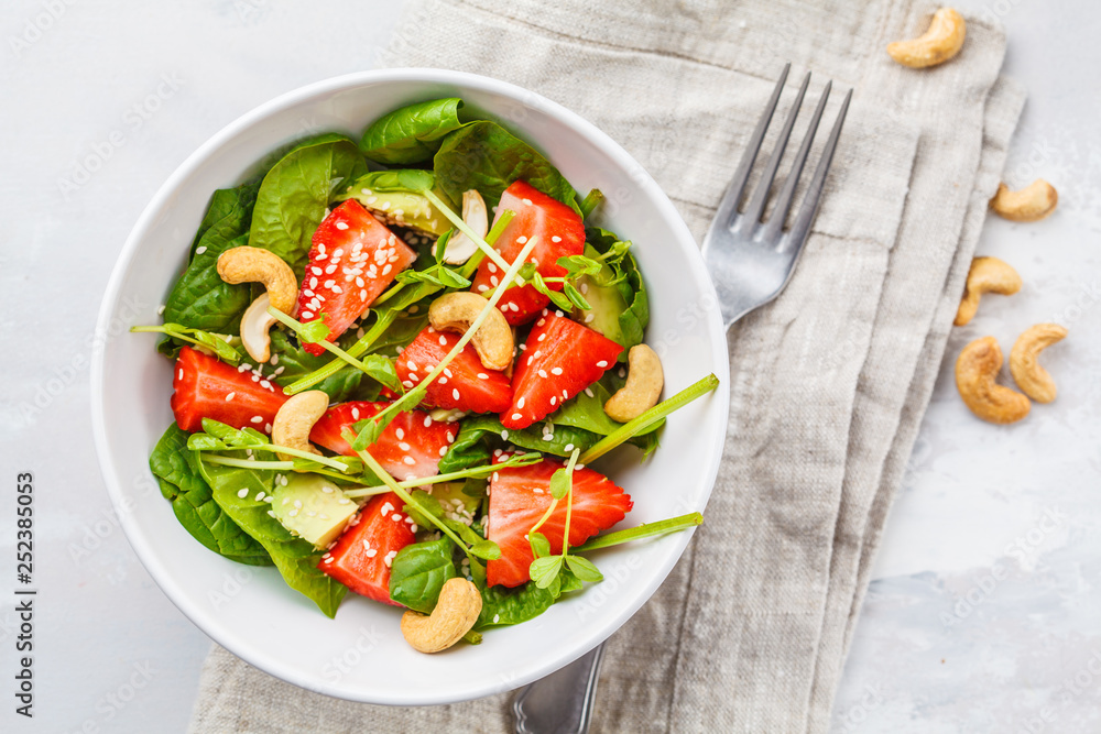 Summer strawberry avocado salad with cashews in a white bowl, top view. Summer strawberry avocado salad with cashews in a white bowl, top view.