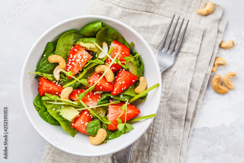 Summer strawberry avocado salad with cashews in a white bowl, top view.