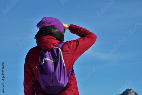 young woman in a jacket and with a backpack looks at the mountains in front