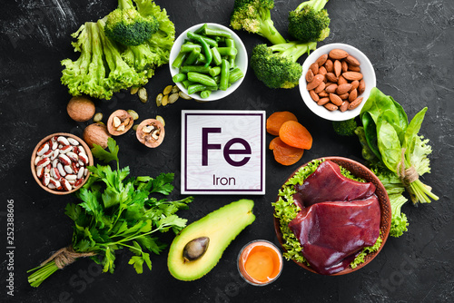 Food containing natural iron. Fe: Liver, avocado, broccoli, spinach, parsley, beans, nuts, on a black stone background. Top view. photo