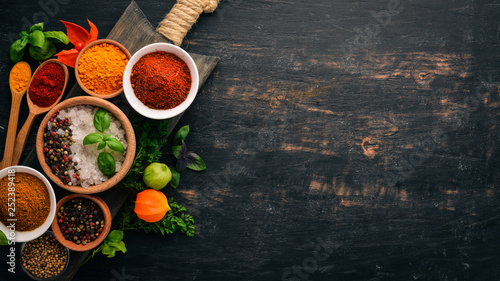 Fototapeta Naklejka Na Ścianę i Meble -  A set of spices and herbs. Indian cuisine. Pepper, salt, paprika, basil, turmeric. On a black wooden chalkboard. Top view. Free copy space.