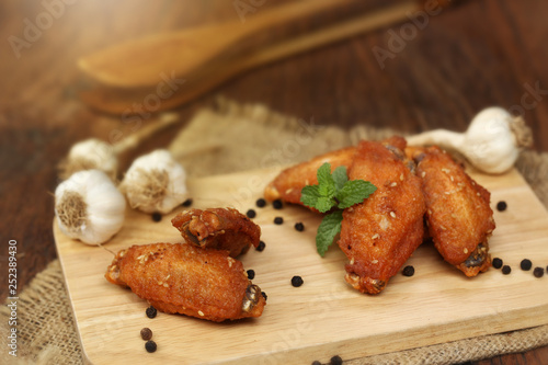 Beautiful plate fried chicken wings on wooden tray with garlic and pepper, selective focus and free copy space. Clean food good taste concept.