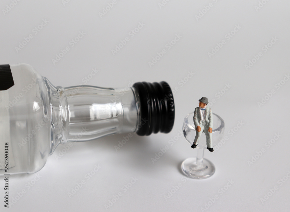 A liquor bottle and a glass. A miniature man sitting on a glass. A liquor bottle and a glass. A miniature man sitting on a glass.