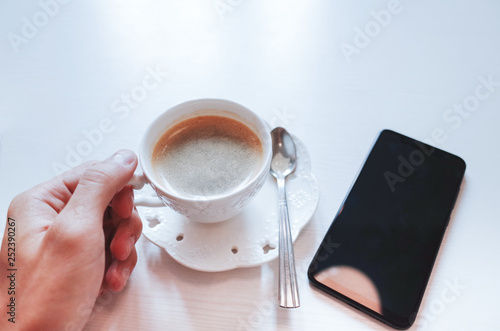 Top view Hand holding of a espresso coffee in white cup with Smart Phone