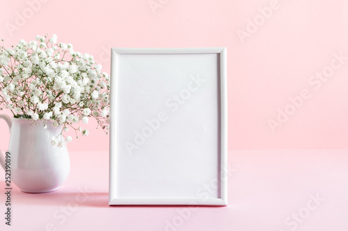 Home interior floral decor. White gypsophila flowers, photo frame. Elegant floral soft pink composition. Beautiful flowers in vase on pastel pink wall background