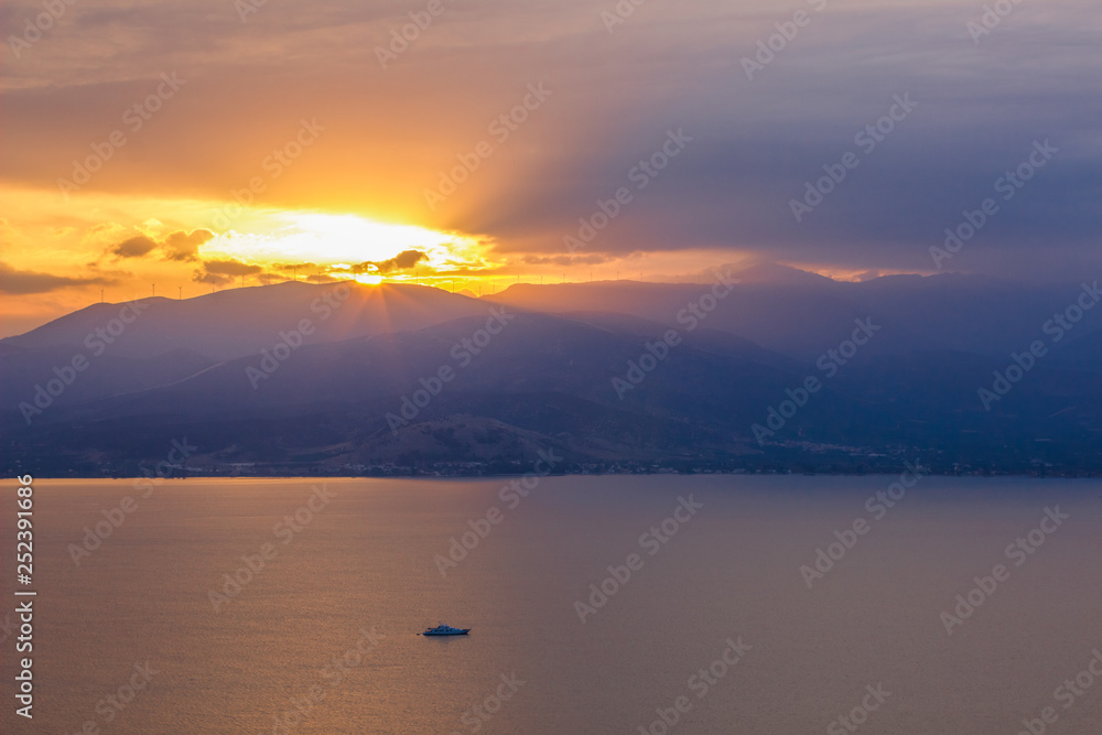 dramatic colorful landscape in sunset time with lake foreground and mountain background with yellow and orange sun rays from above ridge