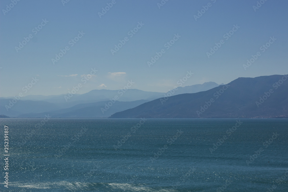 abstract blue landscape of foggy mountain silhouette background and sea foreground 
