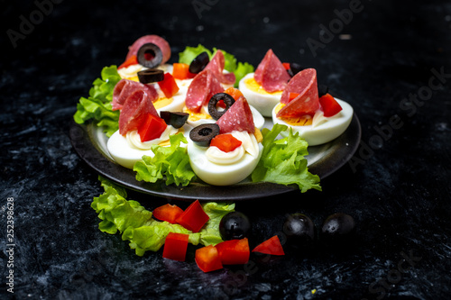 a plate of hard-boiled eggs, with the addition of mayonnaise, green leaves of lettuce, black olives and pieces of salami