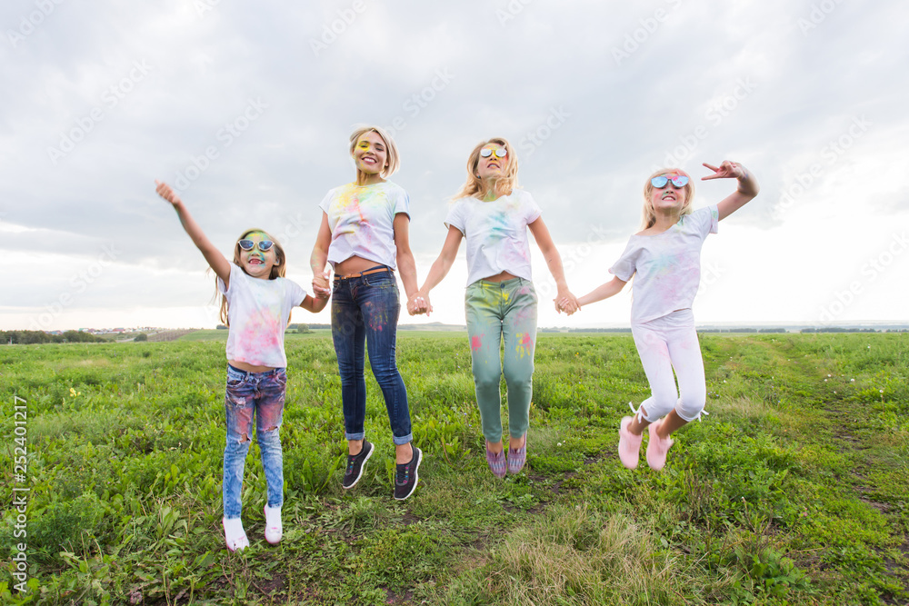 Fun, sisters, festival of holi and holidays concept - Jumping happy mothers and daughters covered in paint Fun, sisters, festival of holi and holidays concept - Jumping happy mothers and daughters covered in paint