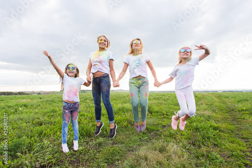 Fun, sisters, festival of holi and holidays concept - Jumping happy mothers and daughters covered in paint
