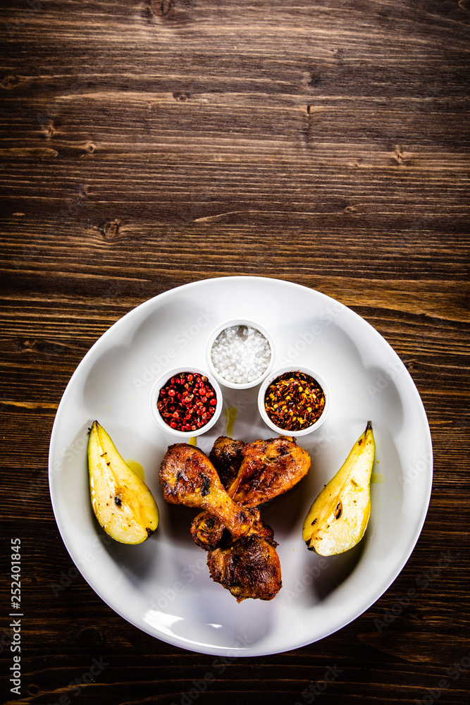 Grilled chicken drumsticks with pear on wooden background