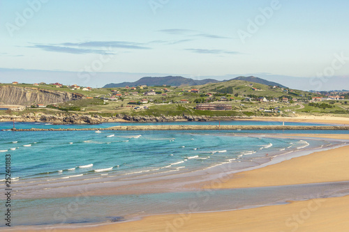 Beautiful Mediterranean seacoast, Cantabria, Spain. Bay, seaside, white foam and teal sea ocean water with small town and walking people