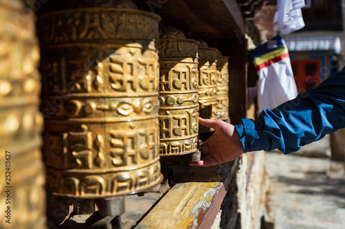 Nepal. Everest trekking. Tibetan prayer wheels in Boudhanath. Hand turns the wheel. On wheels hieroglyphs - prayers in Nepali. Auṃ maṇi padme hūṃ - jewel in the lotus.