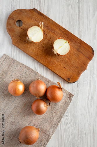 Unpeeled raw yellow onions on a white wooden table, top view. Flat lay, flat lay, from above.
