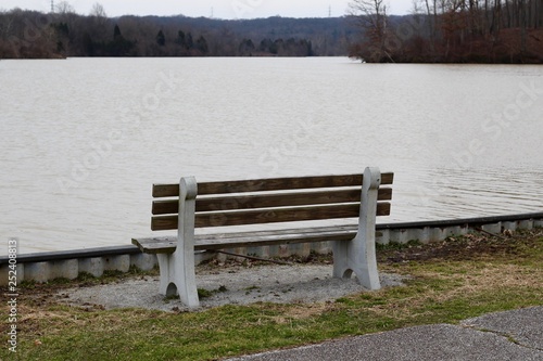 A empty wood park bench near the water of the lake.
