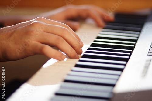 The musician plays a melody, pressing the keys of a modern musical synthesizer, illuminated by weak sunlight