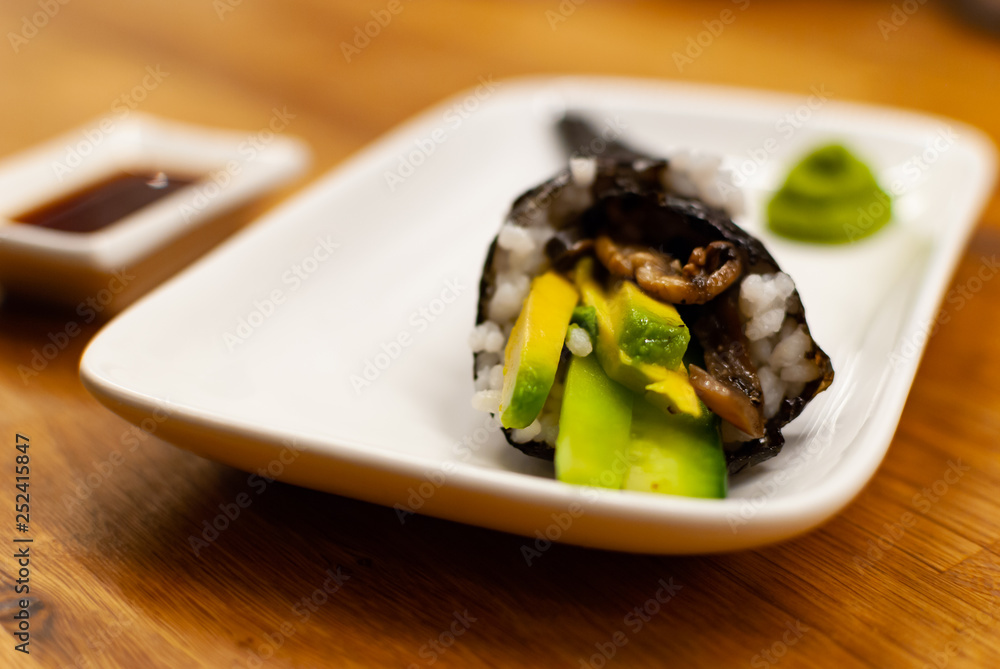Homemade vegan Temaki-Sushi filled with avocado on a small plate on a wooden table with soy sauce and wasabi Homemade vegan Temaki-Sushi filled with avocado on a small plate on a wooden table with soy sauce and wasabi