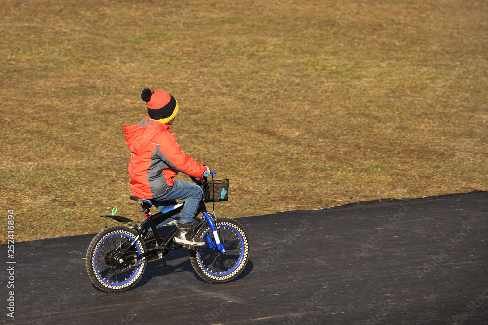 A boy in demi-season clothing rides a bicycle on an asphalt road. The younger generation is engaged in sports and actively spends free time in the fresh air. Games on the street. Children's joy