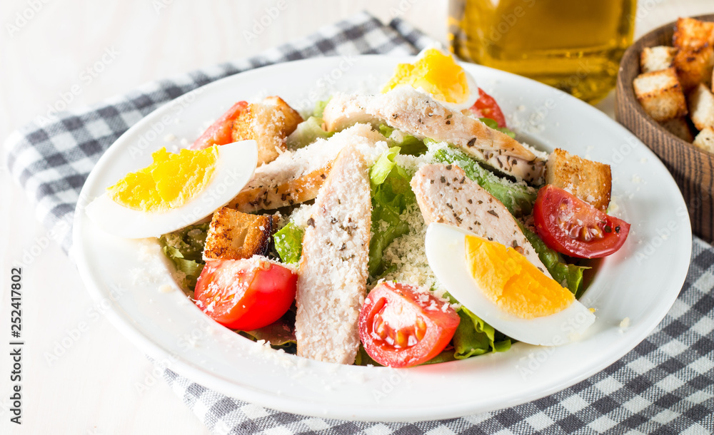 Fresh salad made of tomato, ruccola, chicken breast, eggs, arugula, crackers and spices. Caesar salad in a white, transparent bowl on wooden background