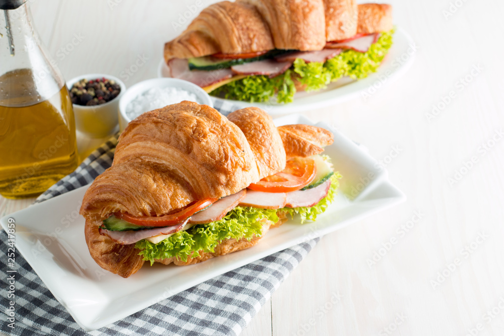 Fresh croissant or sandwich with salad, ham, jamon, prosciutto, salami, cheese, chicken, tomatoes on wooden background. Morning breakfast concept. Healthy and fast food. Fresh croissant or sandwich with salad, ham, jamon, prosciutto, salami, cheese, chicken, tomatoes on wooden background. Morning breakfast concept. Healthy and fast food.
