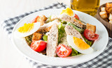 Fresh salad made of tomato, ruccola, chicken breast, eggs, arugula, crackers and spices. Caesar salad in a white, transparent bowl on wooden background