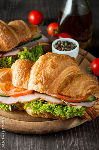 Fresh croissant or sandwich with salad, ham, jamon, prosciutto, salami, cheese, chicken, tomatoes on wooden background. Morning breakfast concept. Healthy and fast food.