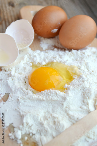 White flour with eggs, butter and wooden spoon on a cooking board