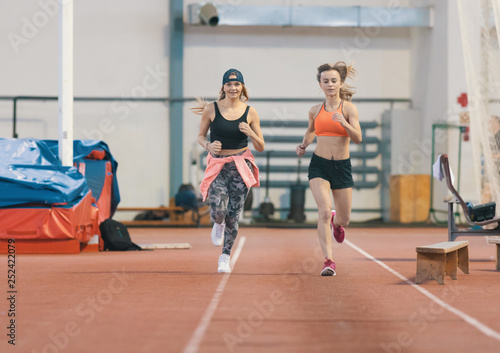 Two young athletic women running in sports arena indoors