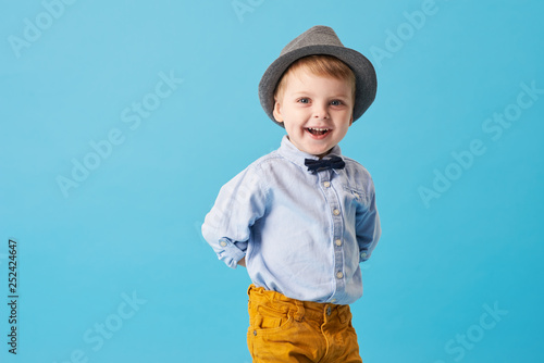 Portrait of happy joyful little boy isolated on blue background. Toddler child in hat and fashionable suit smiling and have a fun 