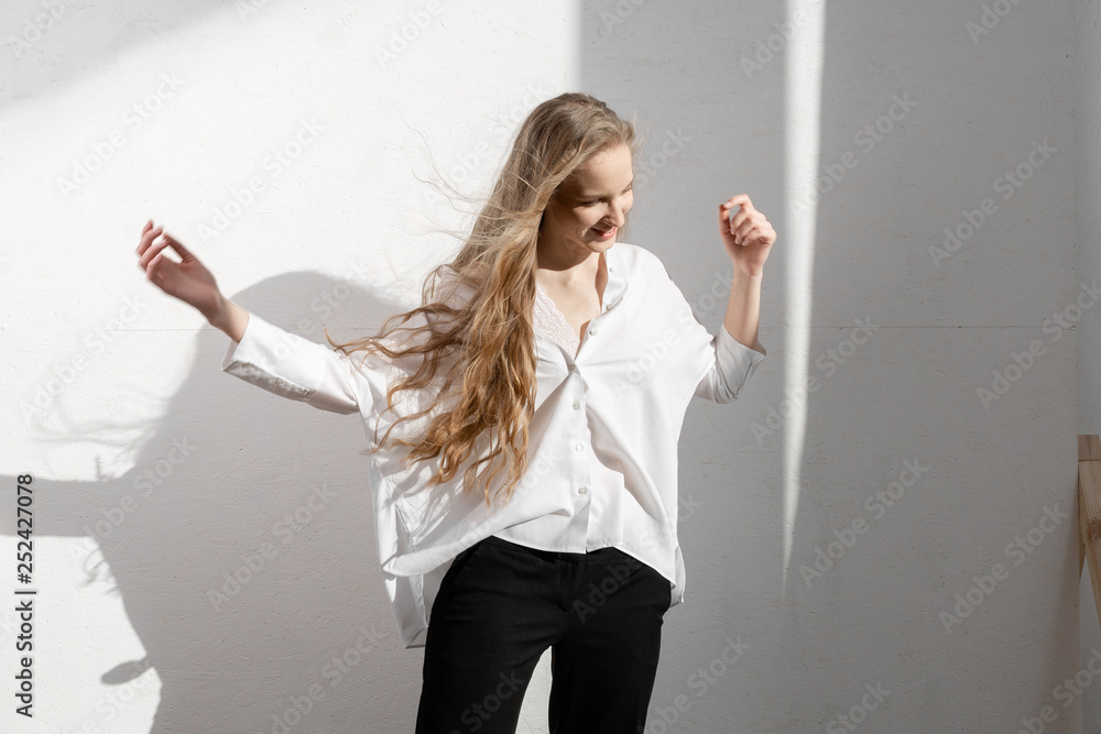 Beautiful fresh blonde model in white shirt and black trousers. Shadows on background Beautiful fresh blonde model in white shirt and black trousers. Shadows on background