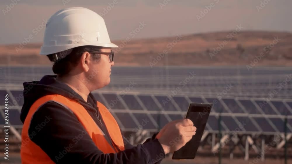 engineer of Asian appearance in an orange vest and hard hat inspects the area after he makes important notes in my tablet engineer of Asian appearance in an orange vest and hard hat inspects the area after he makes important notes in my tablet